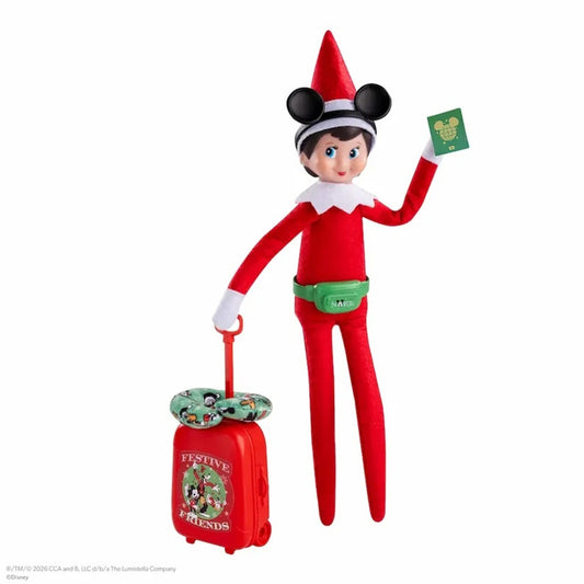 A Disney-themed elf doll dressed in a red outfit with a red hat, black mouse ears, and a green waist bag, standing next to a small red suitcase with a green Mickey-shaped pillow. The elf holds a green card with a Mickey head logo, set against a plain white background.