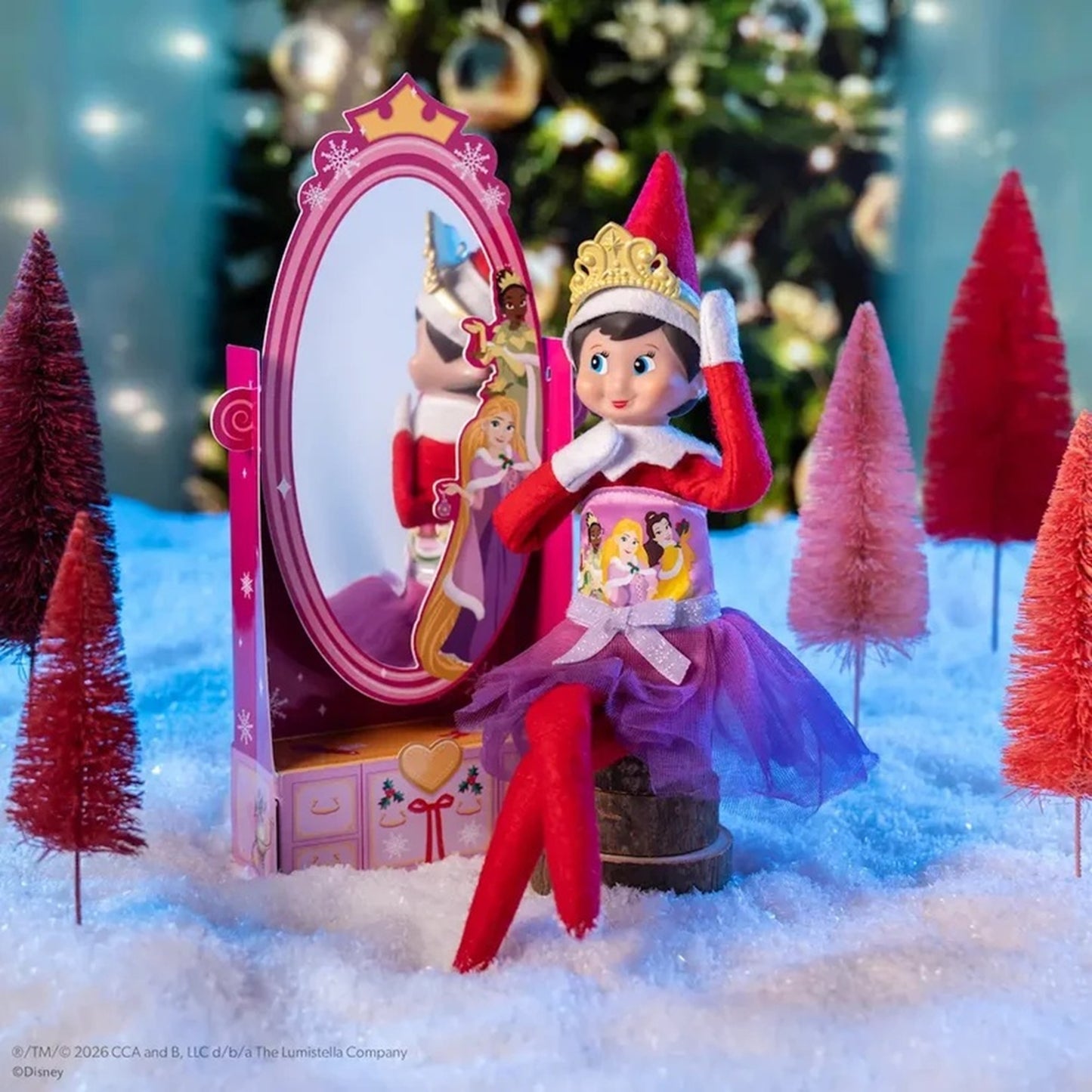 Elf on the Shelf Disney Princess set featuring a doll dressed as Rapunzel sitting in front of a pink vanity mirror, surrounded by miniature Christmas trees on a snowy surface.