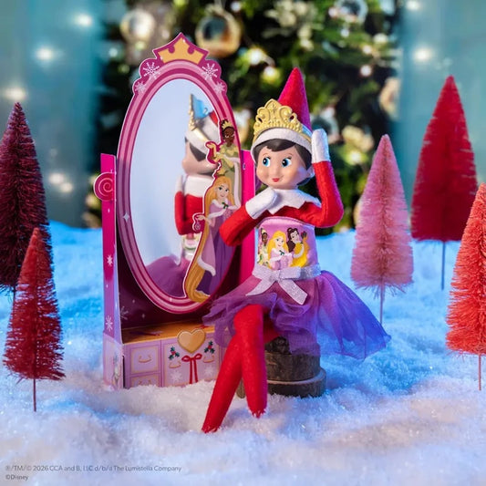 Elf on the Shelf Disney Princess set featuring a doll dressed as Rapunzel sitting in front of a pink vanity mirror, surrounded by miniature Christmas trees on a snowy surface.