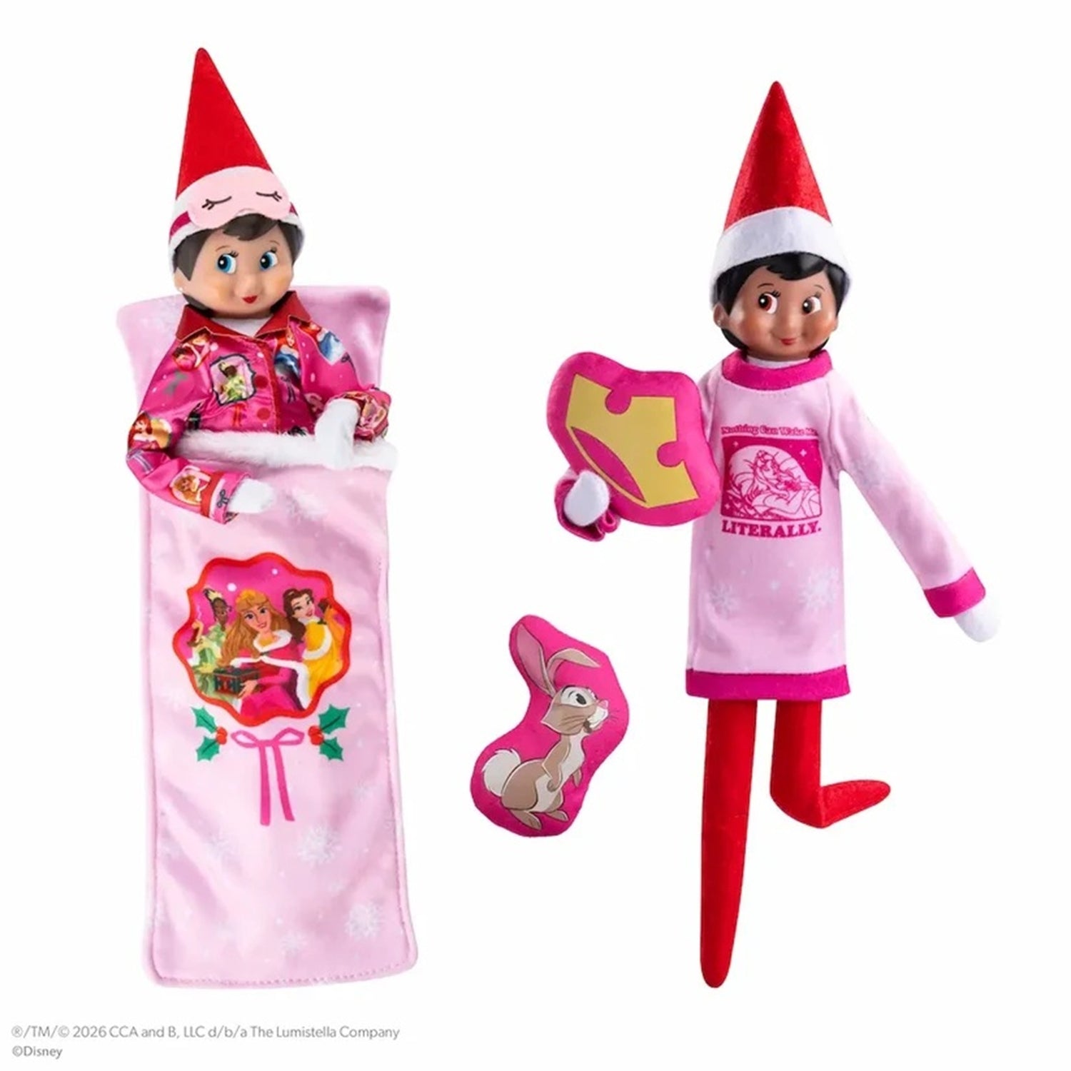 A Disney Elf on the Shelf doll shown in two outfit configurations on a white background: one wrapped in a pink blanket with a lollipop graphic, and one standing in a pink pajama set with a puzzle-piece hat and bunny-shaped accessory.