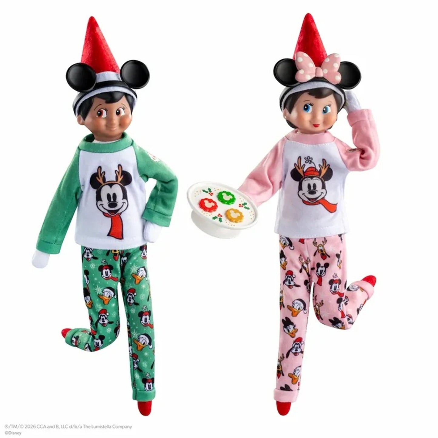 Two children's holiday pajama sets shown on doll-like mannequins against a white background. One set is green with a white chest panel featuring a cartoon face and red scarf motif, paired with green patterned pants.