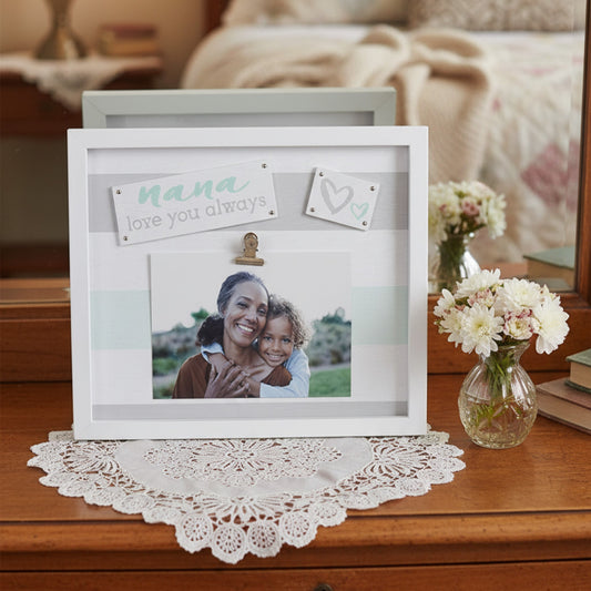 A white rectangular shadow box photo frame with a clip, displayed on a wooden surface with a lace doily. The frame has a personalized card that reads 'nana love you always' and a small heart card.