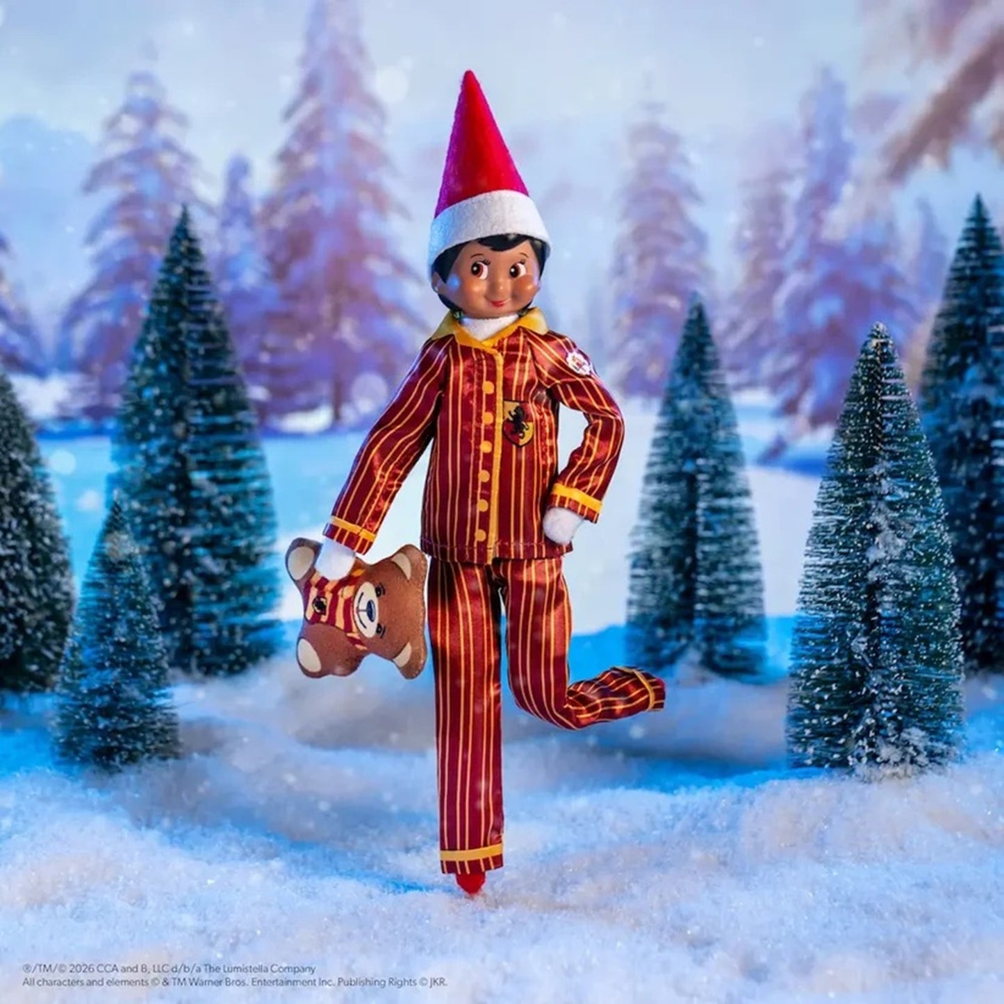 A Christmas-themed action figure dressed in red and gold striped pajamas with a red Santa hat, posed in a snowy forest scene with miniature evergreen trees.