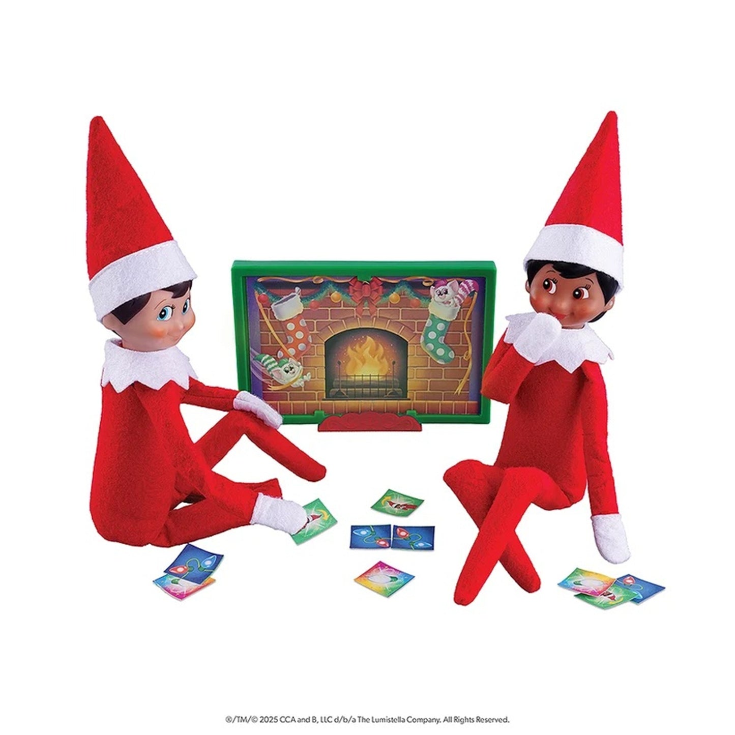 Two Elf on the Shelf dolls wearing red and white outfits sit on either side of a colorful fireplace game board, with small game cards scattered in front, on a white background.