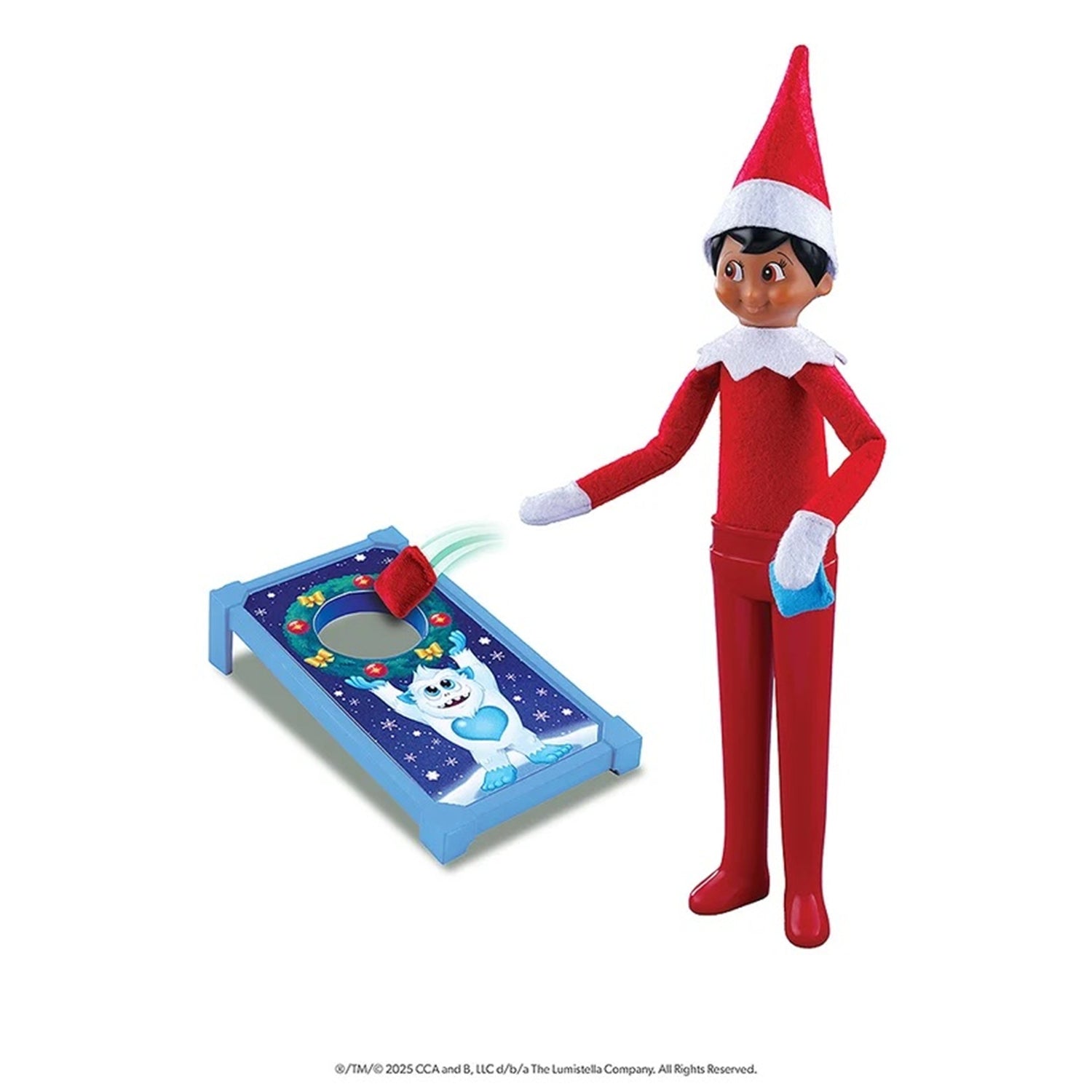Elf on the Shelf toy figure in a red elf suit with a white collar and hat, standing beside a blue cornhole board with a cartoon moon and stars, on a white background.