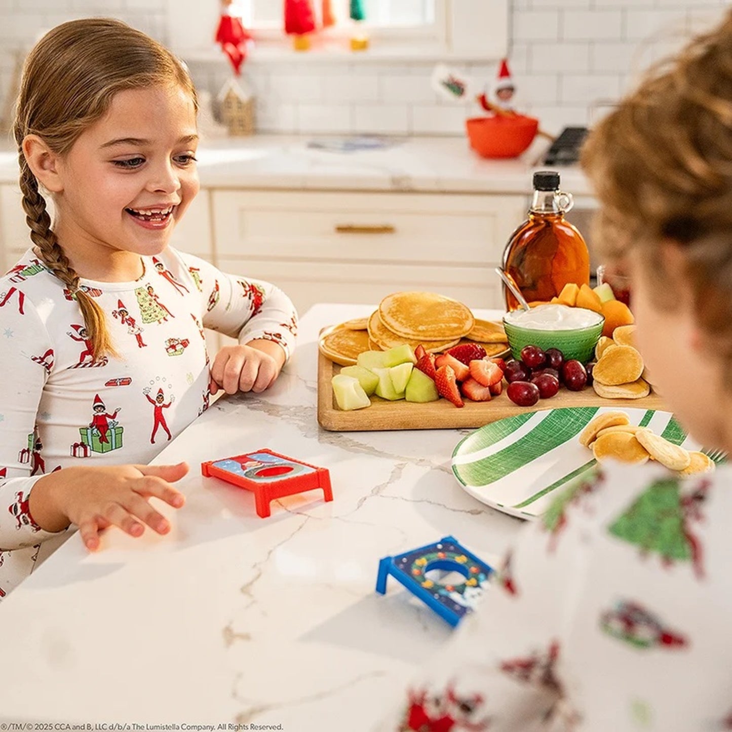 Two children in pajamas at a kitchen table with food and toys.