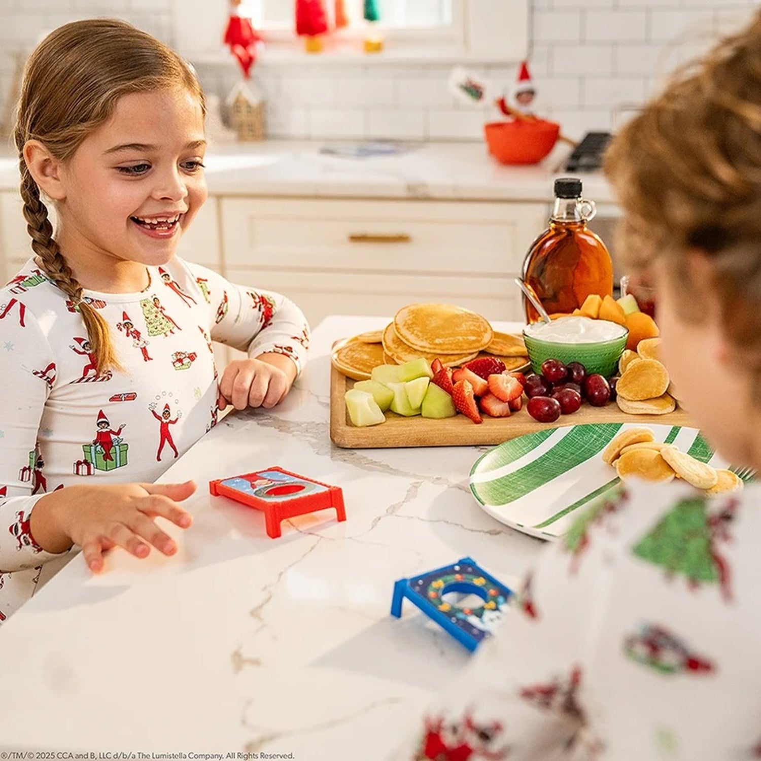Two children in pajamas at a kitchen table with food and toys.